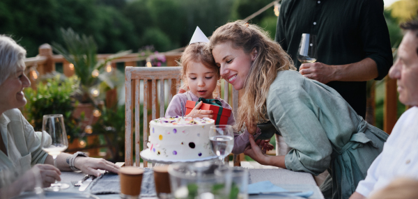 A multi generation family celebratiing birthday of little girl and having garden party outside on patio.