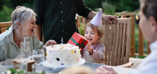 A multi generation family celebratiing birthday of little girl and having garden party outside on patio.