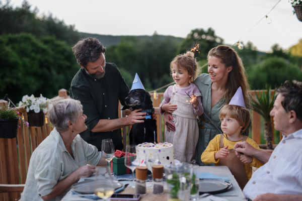 A multi generation family celebratiing birthday of dog and having garden party outside on patio.