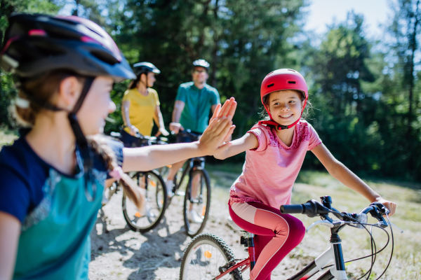 A young family with little children preapring for bike ride, standing with bicycles in nature and high fiving.