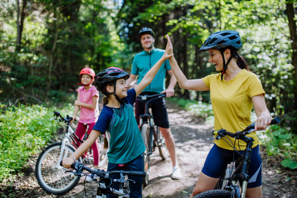 A young family with little children preapring for bike ride, standing with bicycles in nature and high fiving.