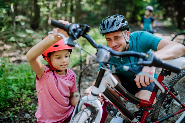 Father chcecking bicycle to her daughter during family trip in a nature.