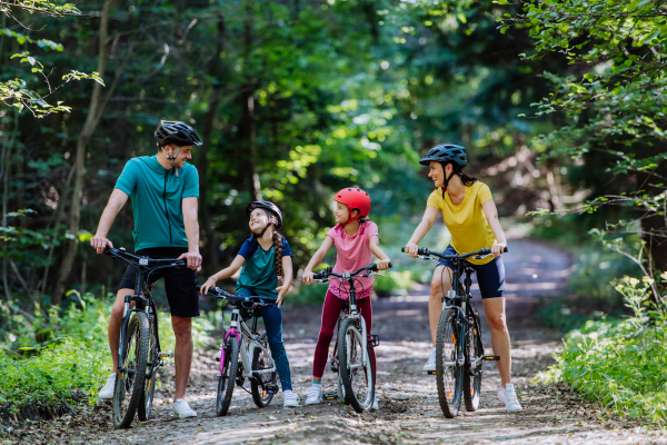 A young family with little children preapring for bike ride, standing with bicycles in nature.