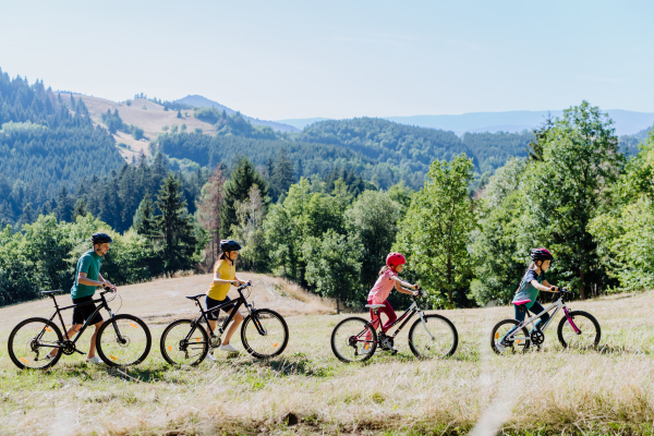 A young family with little child pushing bicycles on trail in nature in summer.