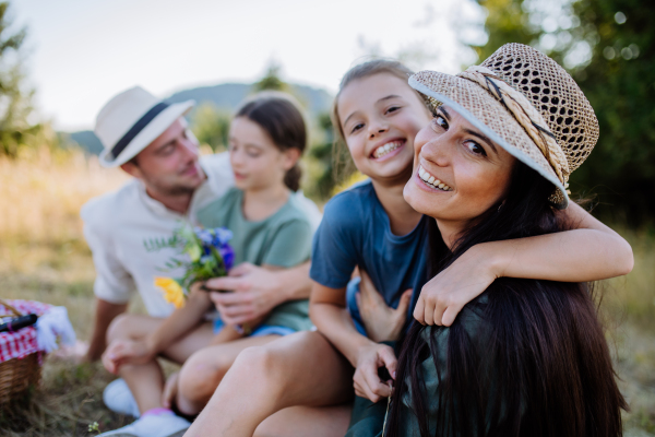 Happy mother and her daughter hugging together during family picnic in nature, sitting at blanket.