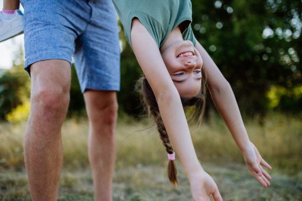 Father swing her daughter, holding her upside down, having fun together in the nature.