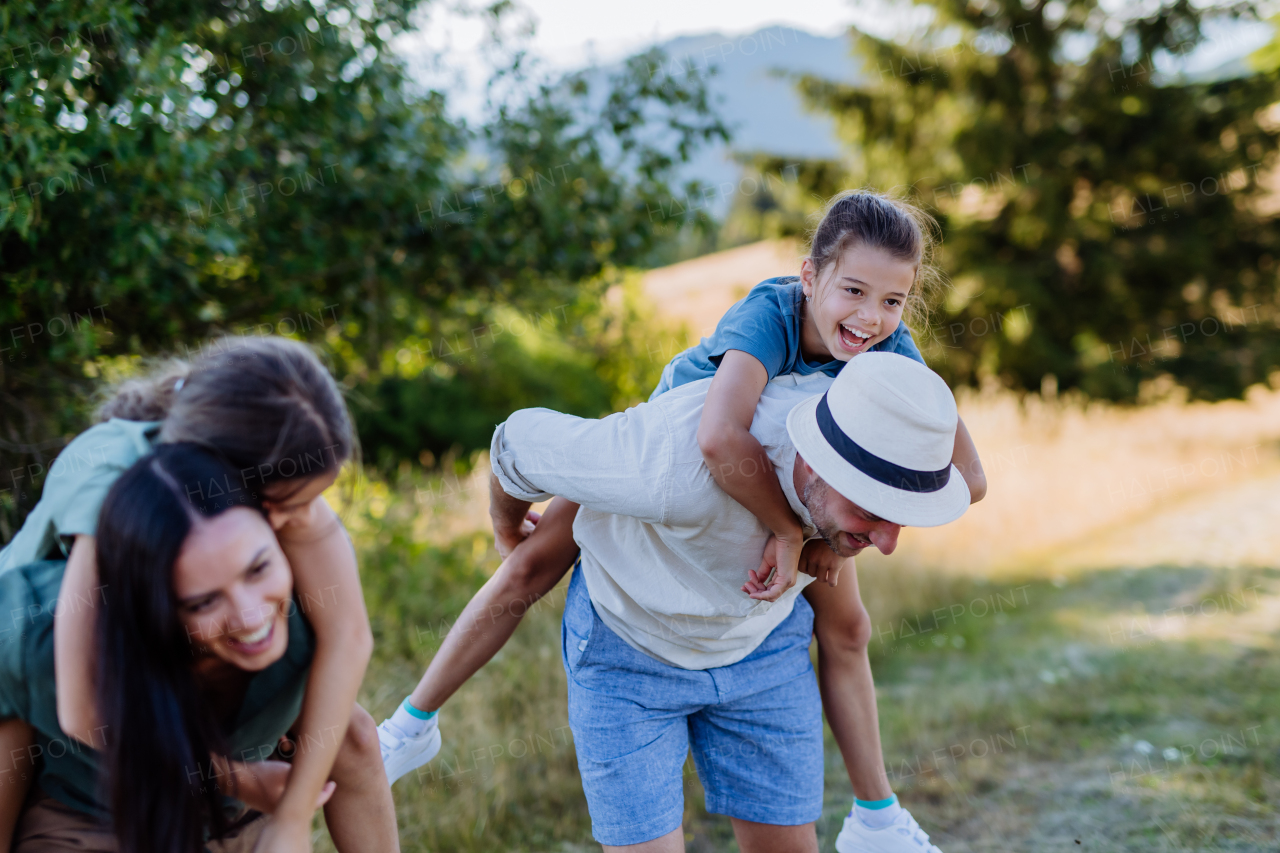 Happy parents giving their children a piggyback ride in summer in nature.