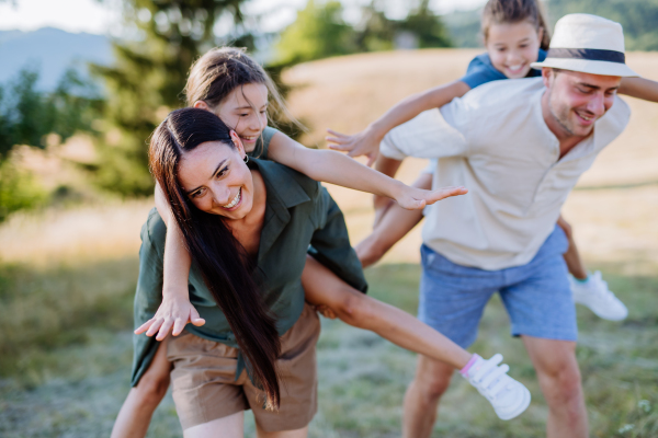 Happy parents giving their children a piggyback ride in summer in nature.