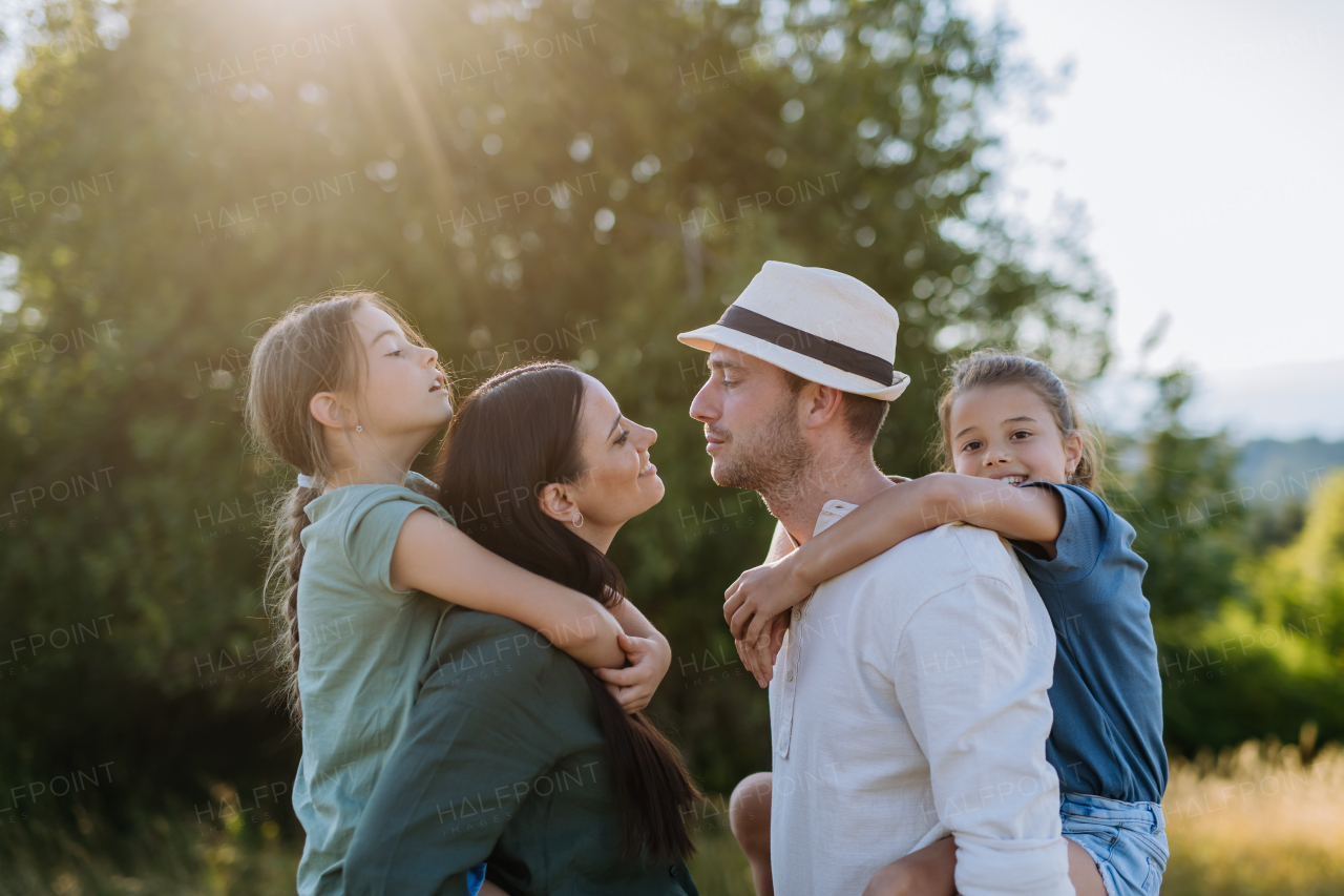 Portrait of young couple with their daughters in nature, kissing. Side view.