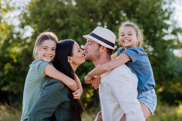 Portrait of young couple with their daughters in nature, kissing. Side view.