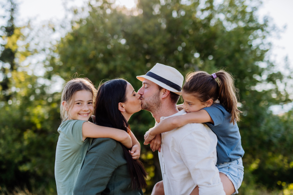 Portrait of young couple with their daughters in nature, kissing. Side view.