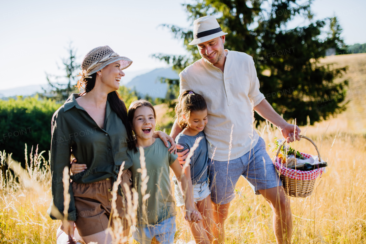 A happy young parents with daughters walking for picnic in nature in summer day.