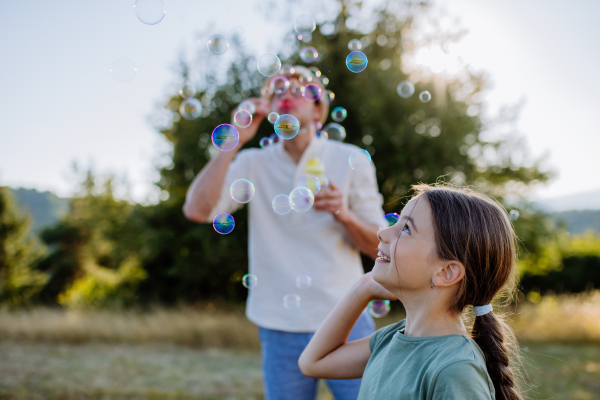 A young father and his little daughter having fun while blowing soap bubbles on a summer day in nature.