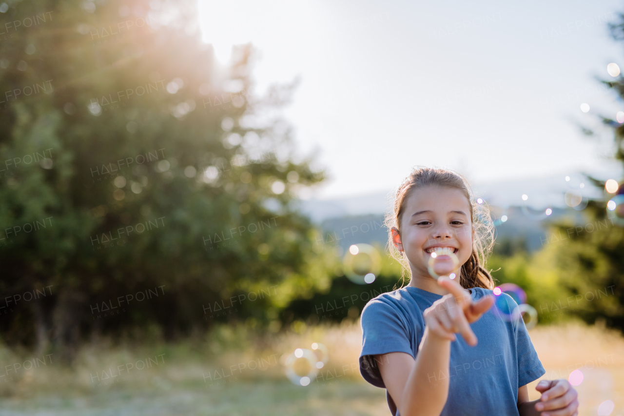 Little girl having fun while blowing a soap bubbles on a summer day in nature.