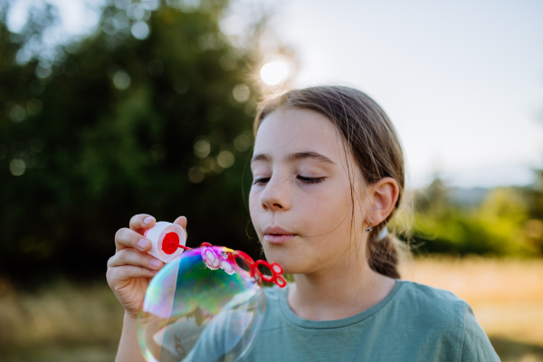 Little girl having fun while blowing a soap bubbles on a summer day in nature.