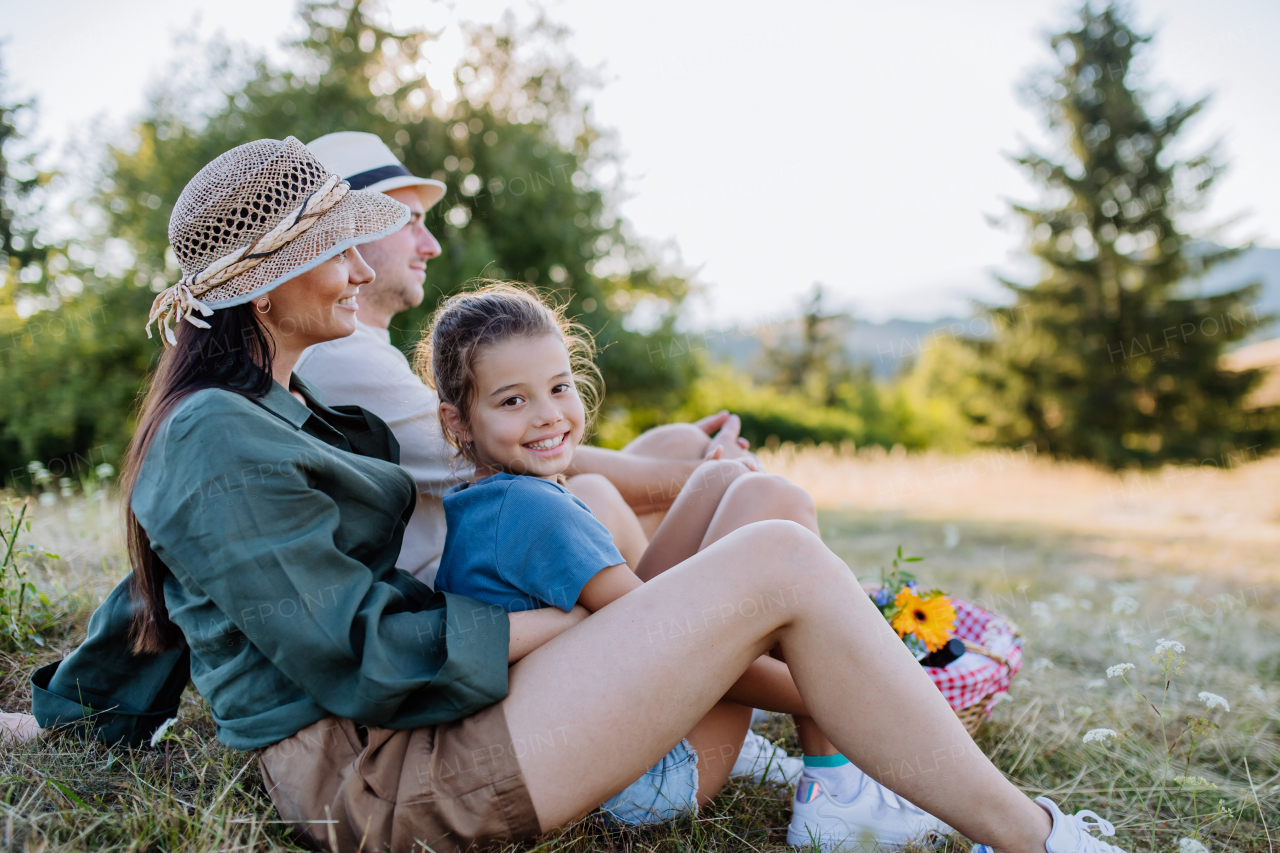 Happy mother and her daughter hugging together during family picnic in nature, sitting at blanket.