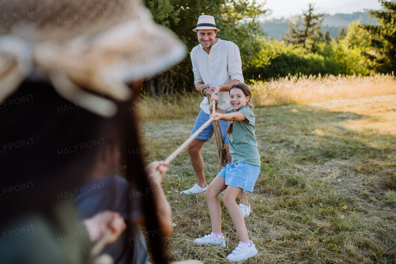 A young family with happy kids having fun together outdoors pulling rope in summer nature.