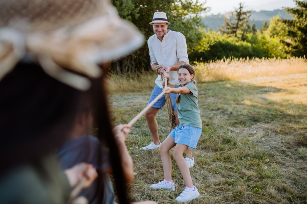 A young family with happy kids having fun together outdoors pulling rope in summer nature.