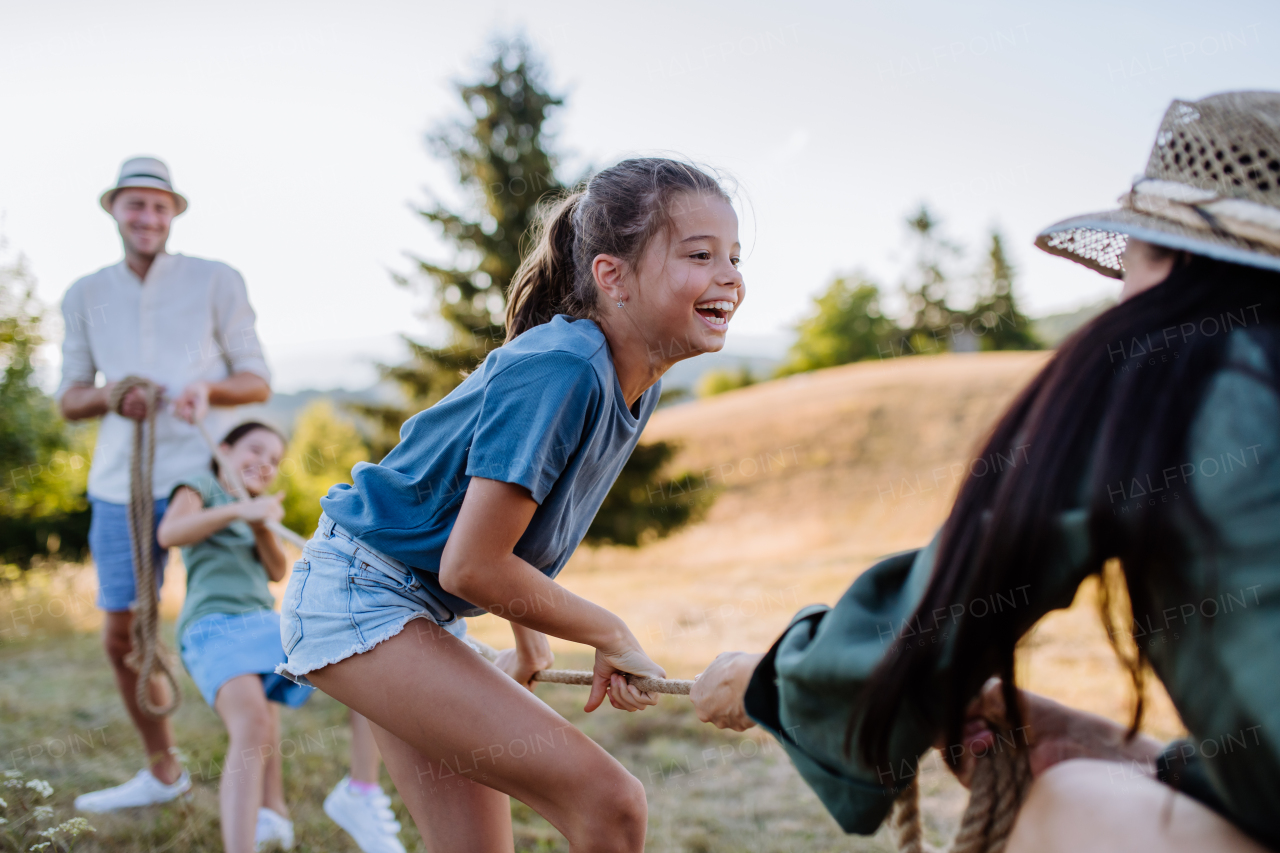 A young family with happy kids having fun together outdoors pulling rope in summer nature.