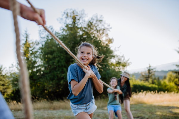 A young family with happy kids having fun together outdoors pulling rope in summer nature.