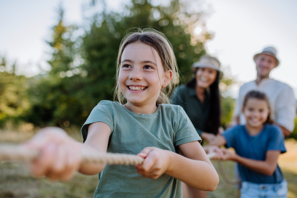 A young family with happy kids having fun together outdoors pulling rope in summer nature.