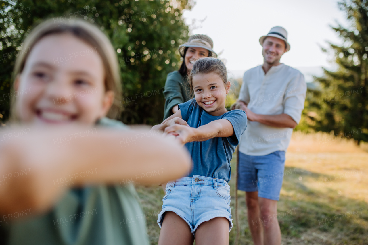 A young family with happy kids having fun together outdoors pulling rope in summer nature.