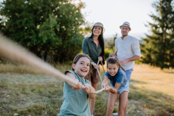 A young family with happy kids having fun together outdoors pulling rope in summer nature.