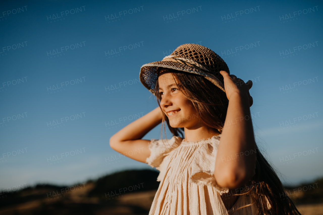 A portrait of a beautiful little girl in summer in nature during sunset.