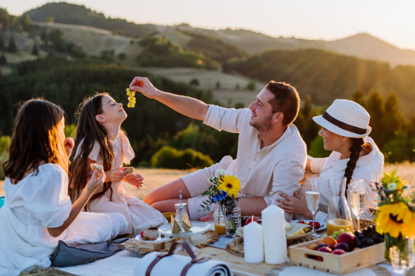 A happy family with children having picnic in park, parents with kids sitting eating healthy meals outdoors.