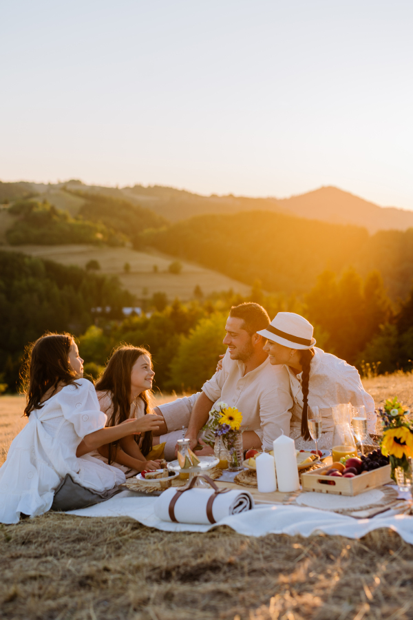 Family with children having picnic in the nature, enjoying sunset.