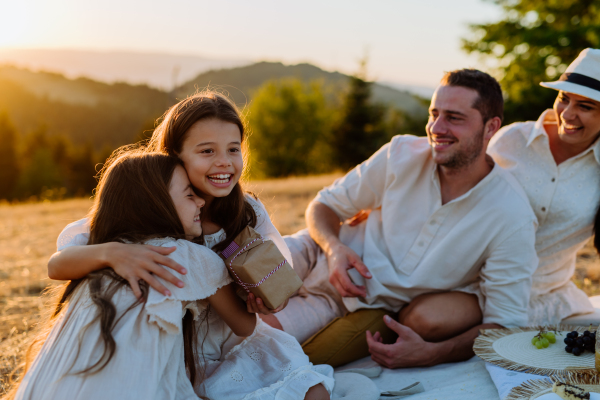 A happy family with children celebrating birthday with gifts outdoors on a picnic in park.