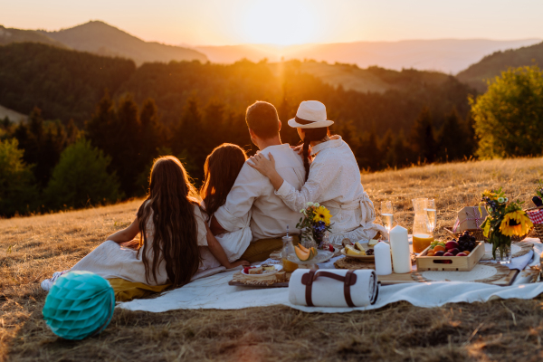 Family with children having picnic in the nature, enjoying sunset. Rear view.