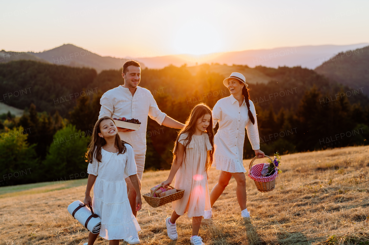 A happy young parents with daughters walking for picnic in nature in summer during sunset.