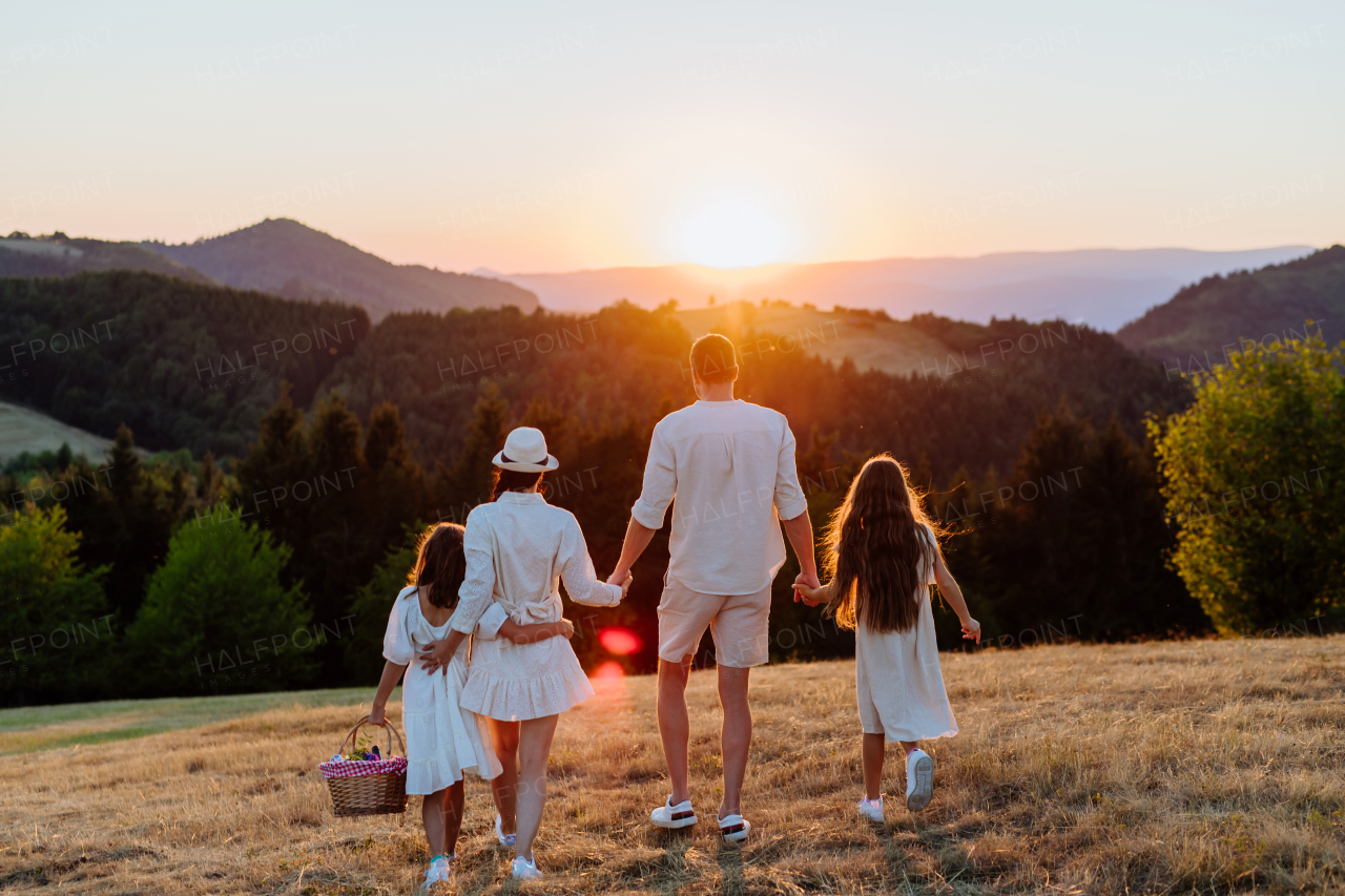 A happy young parents with daughters walking for picnic in nature in summer day.