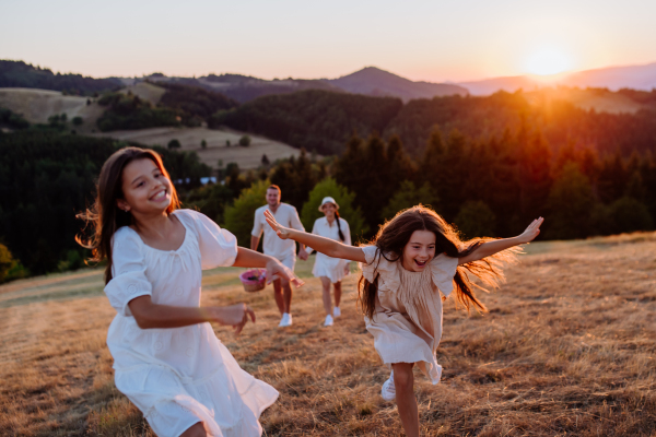 A happy young parents with daughters walking for picnic in nature in summer during sunset.