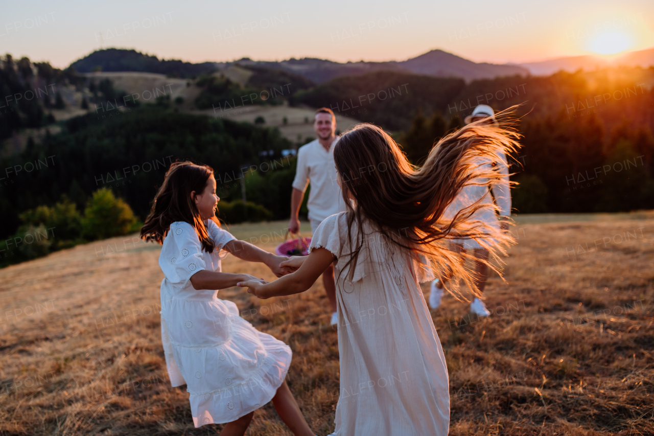 A happy young parents with daughters walking for picnic in nature in summer during sunset.