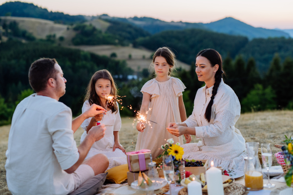 Happy family with children having picnic in the park, clebrating with sparklers.