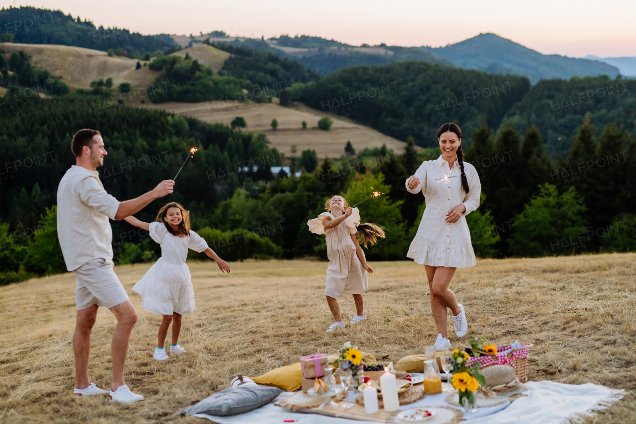 Happy family with children having picnic in the park, clebrating with sparklers.