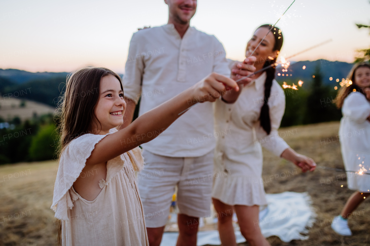 A young family with children together with sparklers enjoying picnic party in nature in summer.