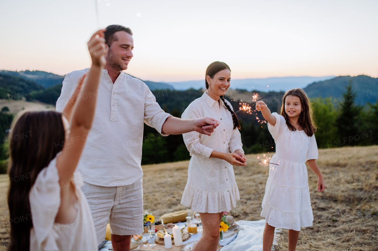 Happy family with children having picnic in the park, clebrating with sparklers.