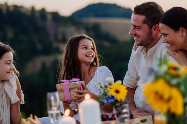 A happy family with children celebrating birthday with gifts outdoors on a picnic in park.