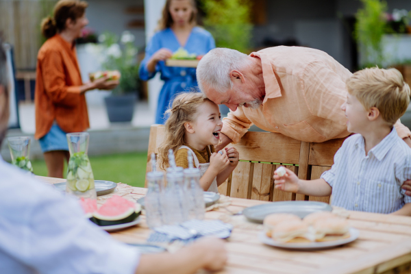 A multi generation family having garden party celebration, grandfather is entertaining grandchildren, laughing and having fun.