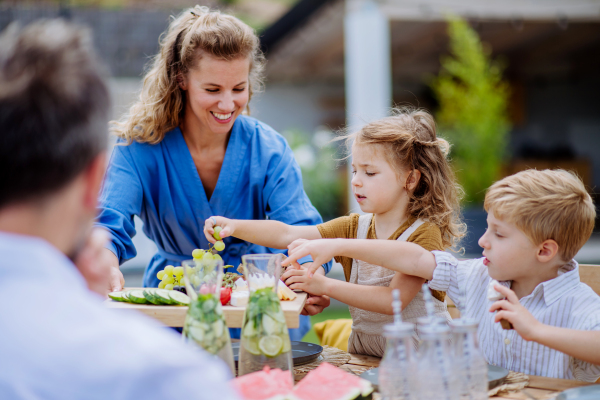 A family having garden party celebration, children are eating snacks, laughing and having fun.