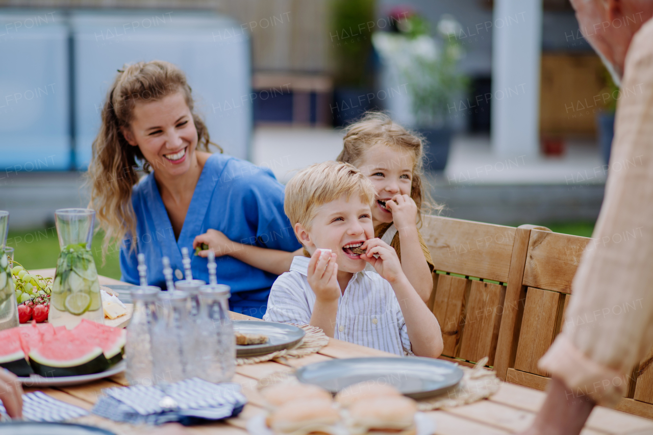 A multi generation family having garden party celebration, grandfather is entertaining grandchildren, laughing and having fun.