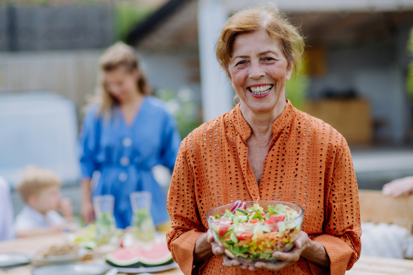 A happy senior woman serving salad at multi generation garden party in summer.