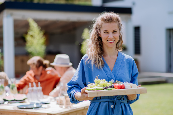 Portrait of young woman holding tray with snack for garden party.