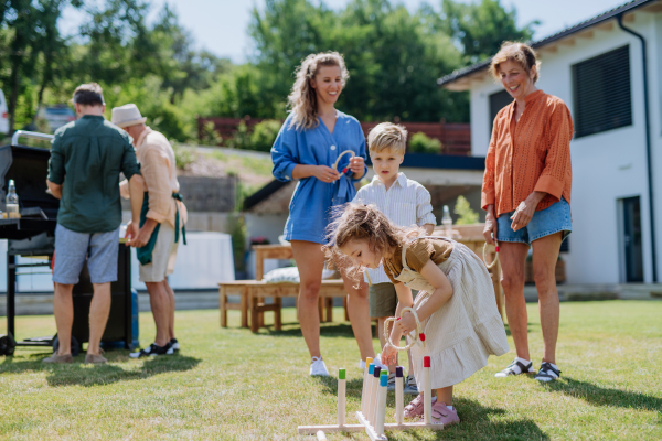 A multi generation family playing throw a ring game when grilling outside on backyard in summer at garden party.