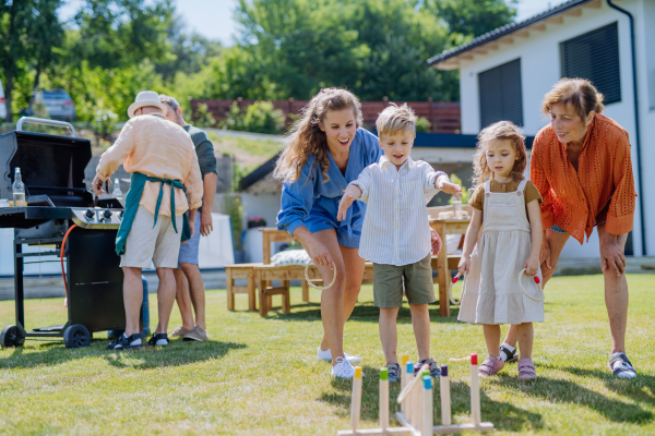 A multi generation family playing throw a ring game when grilling outside on backyard in summer at garden party.