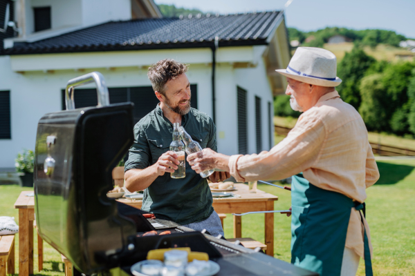 A senior father with adult son grilling outside on backyard in summer during family garden party.