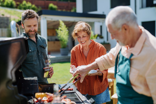 A multi generation family grilling outside on backyard in summer during garden party